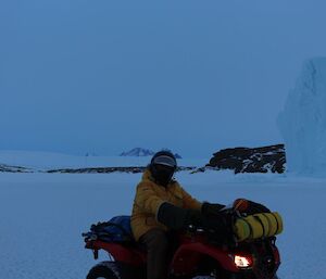 A man on a quad in front of an iceberg.