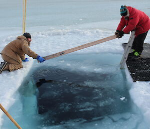 2 men skim ice of a hole in the frozen sea ice