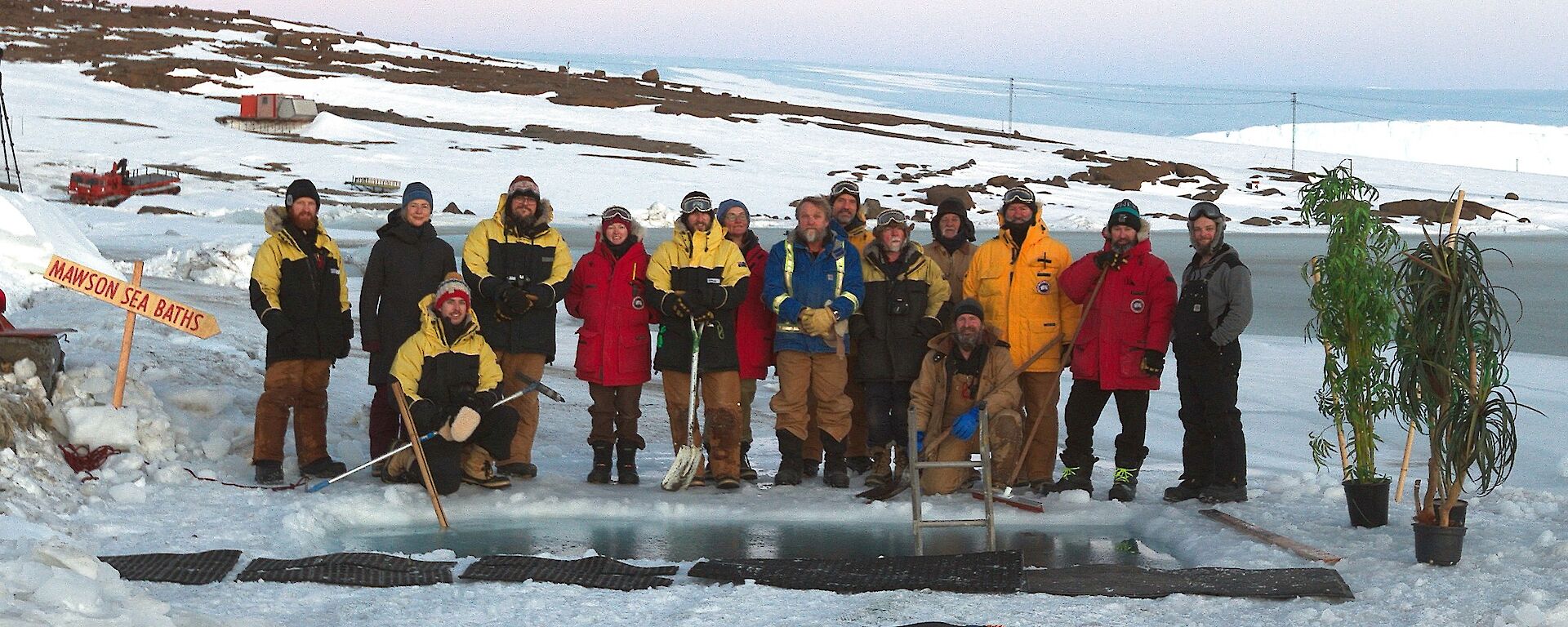 A group of people in winter clothes around a swimming hole in the ice