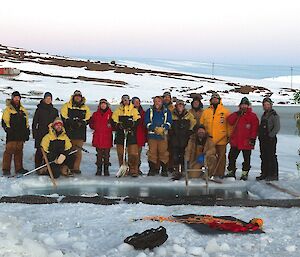 A group of people in winter clothes around a swimming hole in the ice