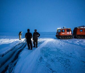 A man drills the sea ice as 2 others look on