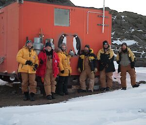 A group of men stand outside a field hut