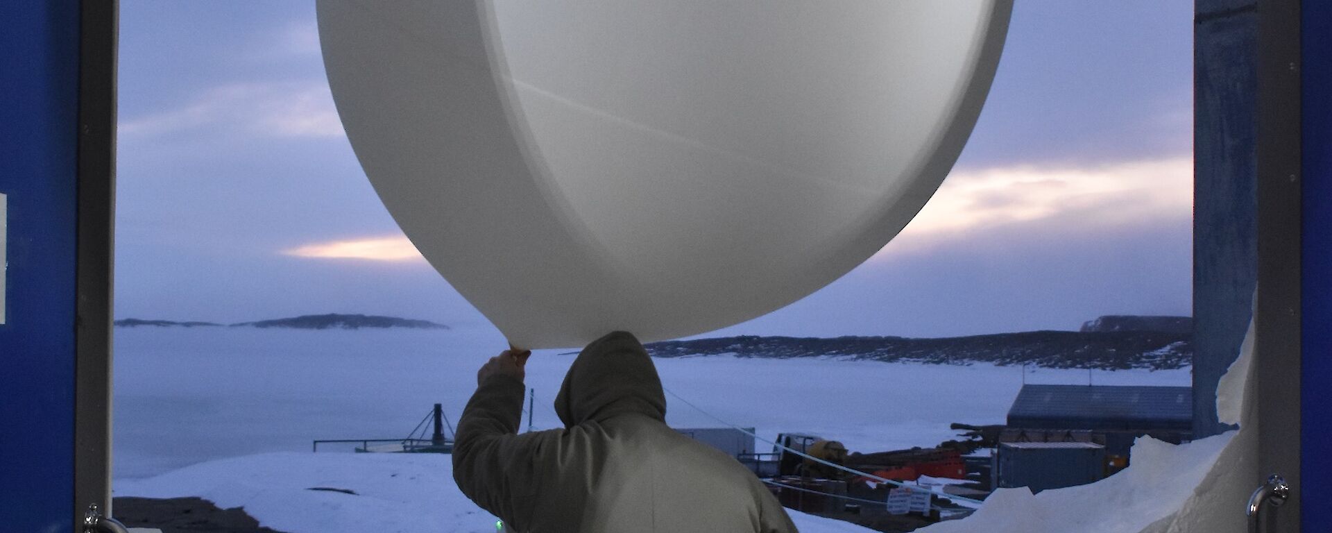 A man exits a building with a weather balloon