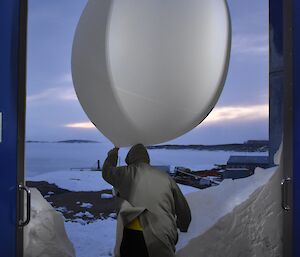 A man exits a building with a weather balloon