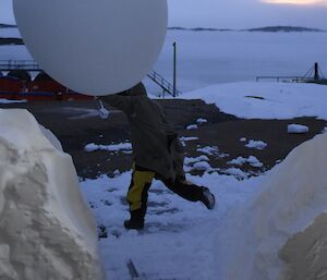 A man exits the buildin with a weather balloon