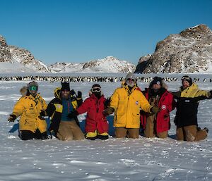 Group of people standing together with penguins in background.