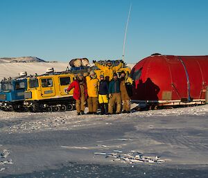 Group of people standing together in front of hut.
