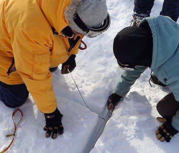 Two people set a snow anchor