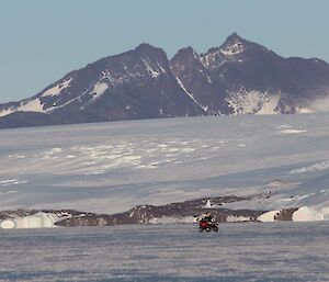 A wuad bike travelling on sea ice in front of a mountain range