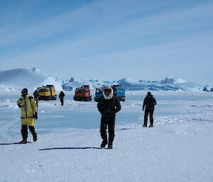 A group of people walk away from the vehicles near some icebergs