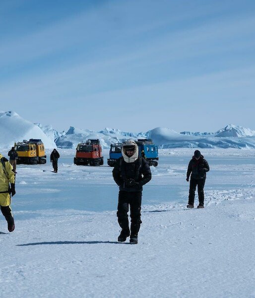 A group of people walk away from the vehicles near some icebergs