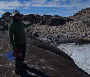 A woman points to the penguin colony behind her