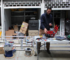 Christian Schoof stands at a table in a shed with a camera and pelican case and a range of cords and wires.