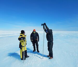 Scientists drilling a hole in the glacier ice with a very long (two metres plus), thin metal drill bit.