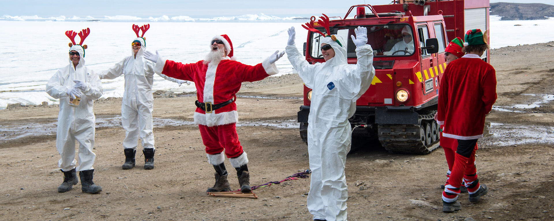 Expeditioners dresses as Santa and three elves in white, with a hagglund vehicle, on the Davis station foreshore.