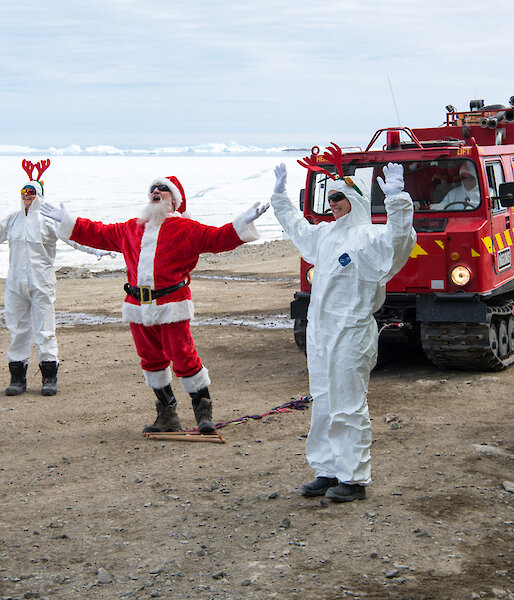 Expeditioners dresses as Santa and three elves in white, with a hagglund vehicle, on the Davis station foreshore.