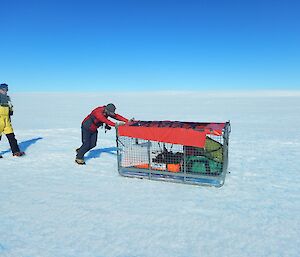 Expeditioner pushing a crate of bags and equipment across the ice.