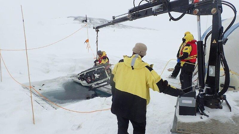 A small crane lowers the remotely operated vehicle into a hole in the fast ice.