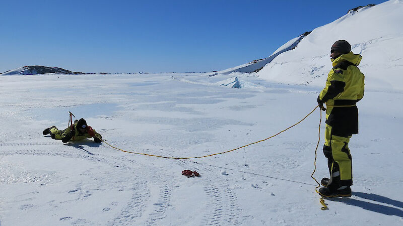 Two expeditioners practicing sea ice rescue techniques on the ice.