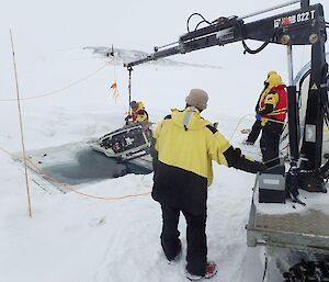 A small crane lowers the remotely operated vehicle into a hole in the fast ice.