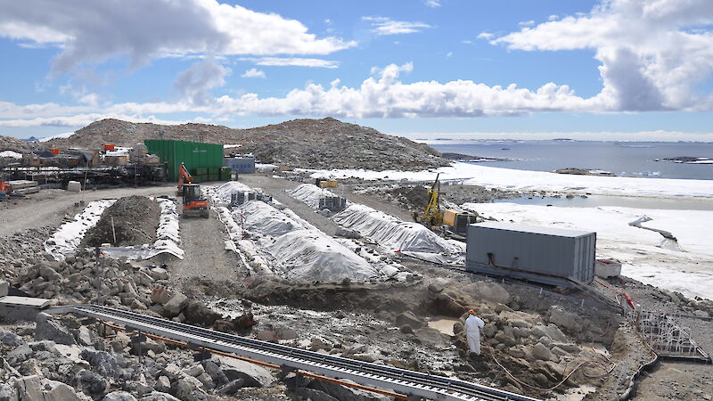 Remediation at the Main Power House fuel spill site. Contaminated soil is being excavated in front of the permeable reactive barrier (lower right of photo) and placed into biopile 6. Biopiles 1–5 can be seen with their covers on. Aeration systems are visible between the biopiles.