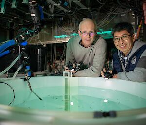 Two men looking in to a circular tank containing krill.