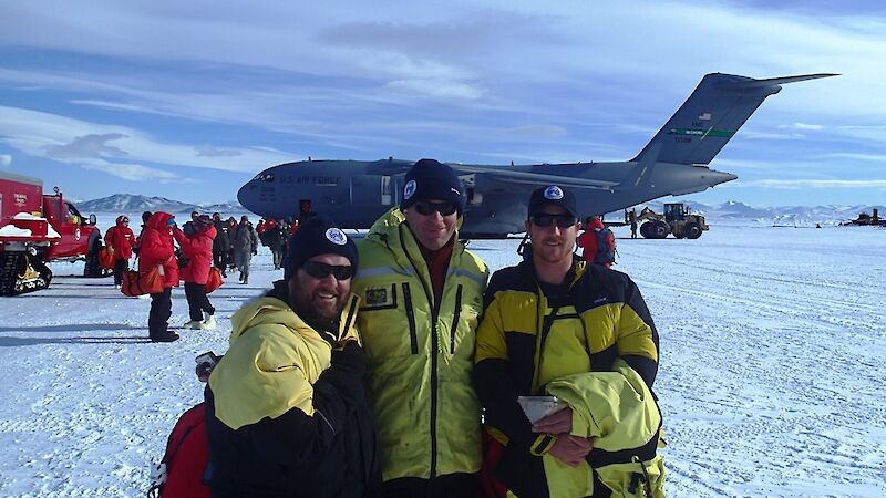 Three of the project team members stand in front of the Hercules aircraft in Antarctica