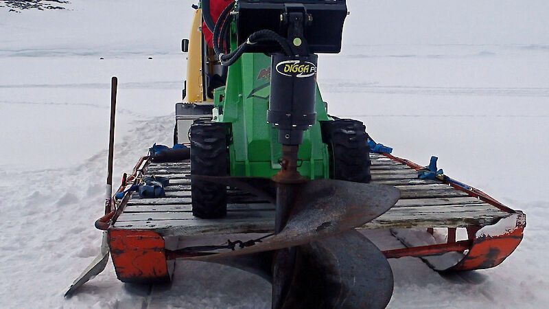 An expeditioner uses a special drill attachment on a small tractor to drill a dive hole in the sea ice