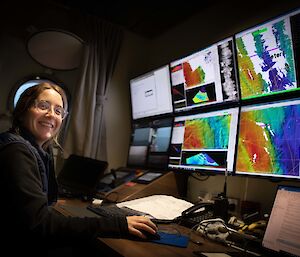 A technician sits in front of a bank of computer screens displaying colourful maps of the sea floor.