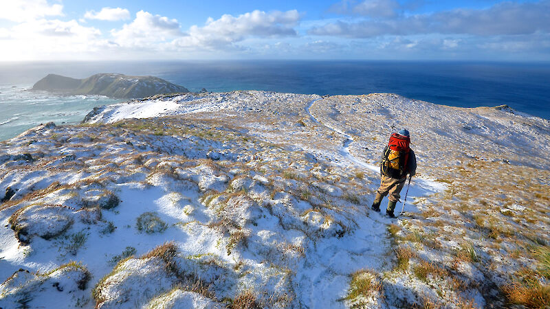 Expeditioner standing with back to camera as he takes in the view north on snow covered plateau to Wireless Hill and North Head.