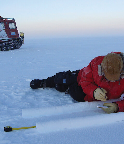 Scientists lying on the ice while marking long ice core samples