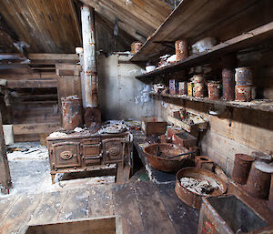 Inside the Main Hut after conservators have cleared it of ice. Visible are shelves of tinned goods and a rusty stove.