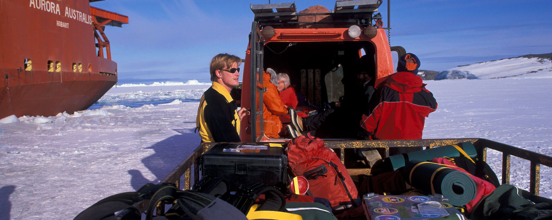 Robb standing on the sea ice next to the ship Aurora Australis, with a trailer full of expedition kit.