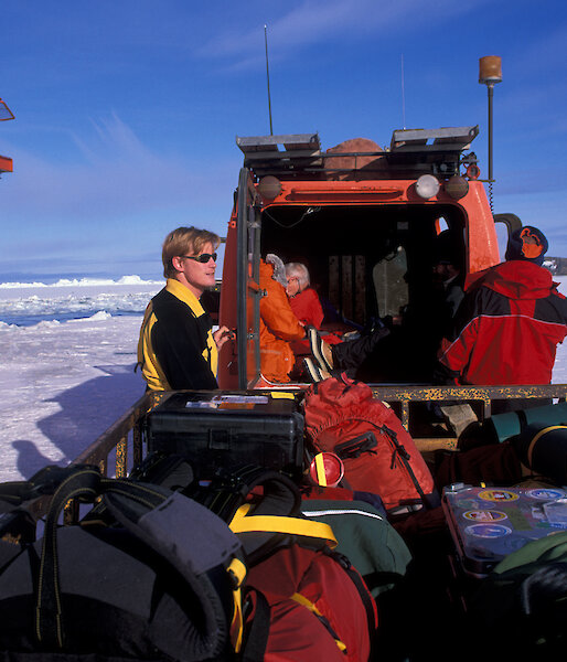 Robb standing on the sea ice next to the ship Aurora Australis, with a trailer full of expedition kit.