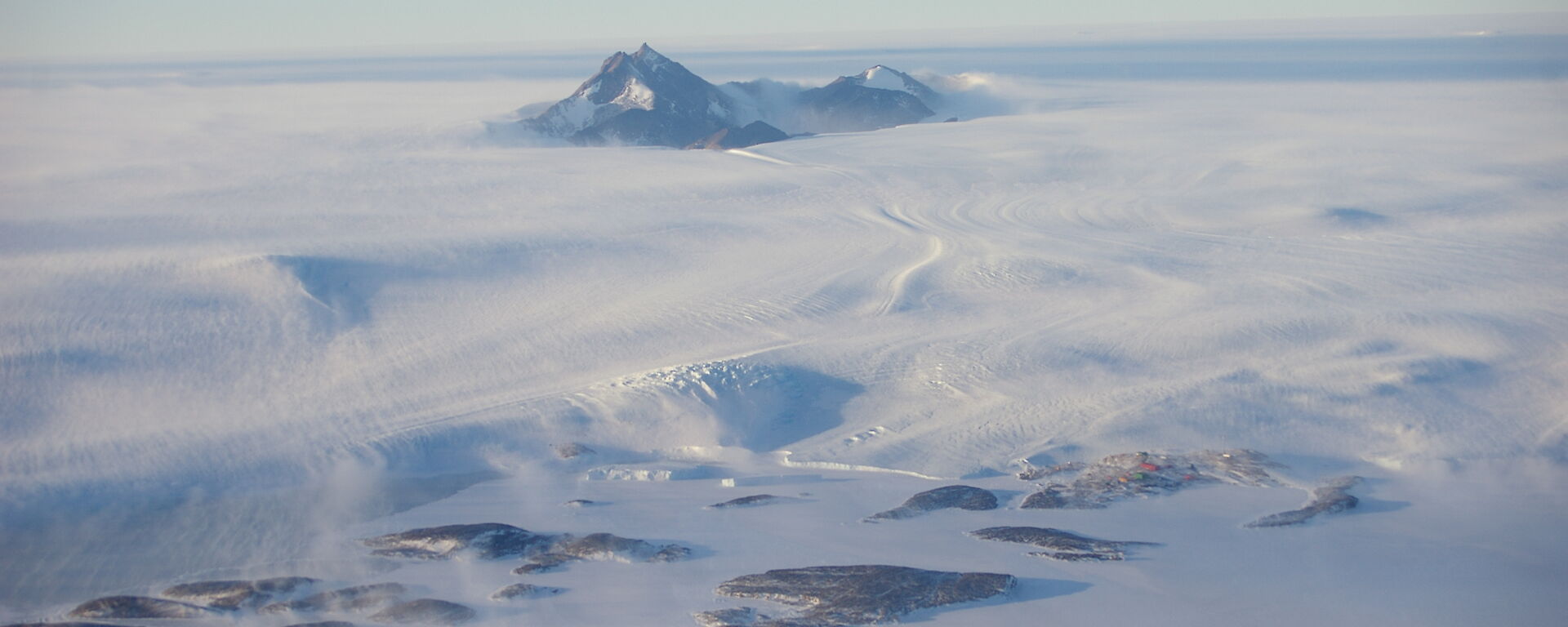 View of wind driven snow from a helicopter over rocky peaks near Mawson.