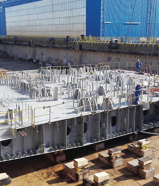 Placement of four conjoined blocks encompassing the deck forward of the engine room and the moon pool hull aperture, within the dry dock.