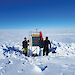 Scientists standing beside semi-buried scientific equipment on the Totten Glacier.