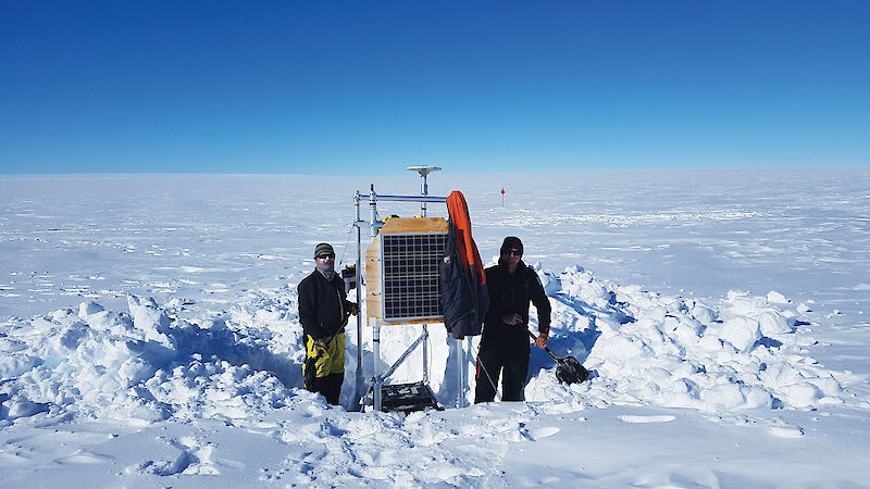Scientists standing beside semi-buried scientific equipment on the Totten Glacier.