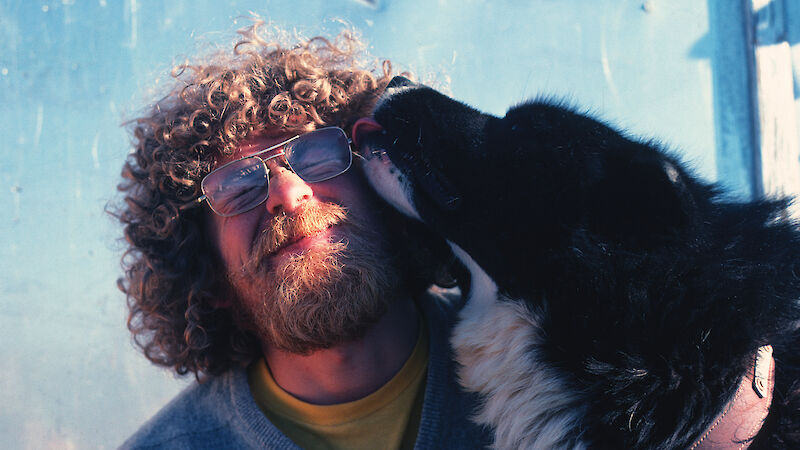 Tom Maggs at Mawson with a husky licking his face.