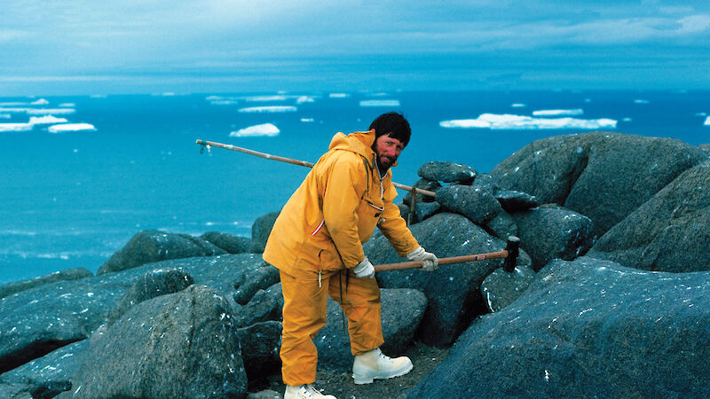 Bob Tingey hitting a rock in Antarctica with a long handled hammer.