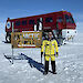Director Kim Ellis standing next to the Antarctic Circle sign with the red Terra Bus behind.