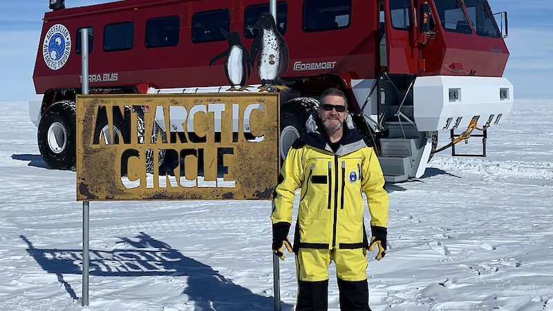 Director Kim Ellis standing next to the Antarctic Circle sign with the red Terra Bus behind.