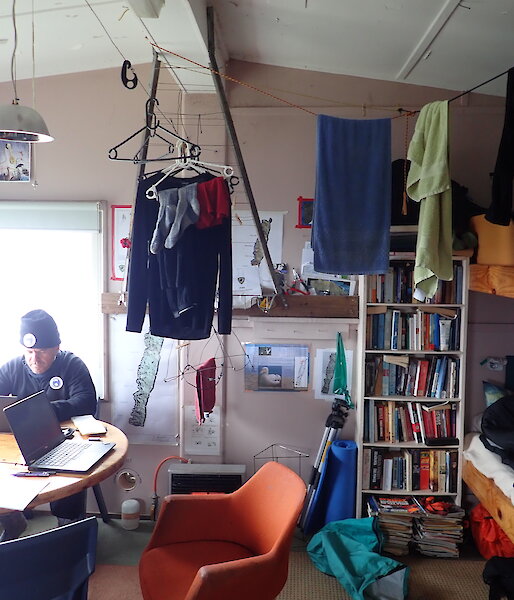 The inside of Hurd Point hut showing bunks, bookshelf and kitchen table, and clothes strung up to dry.