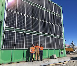 Carpenters Conrad Willersdorf and Paulie Hanlon, and Engineering Services Supervisor Doreen McCurdy, stand outside the green store with the completed panel installation on the wall behind.