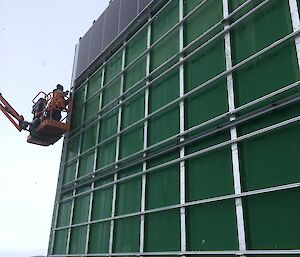 Two installers use the elevated work platform to attach solar panels to the north wall of the green store.