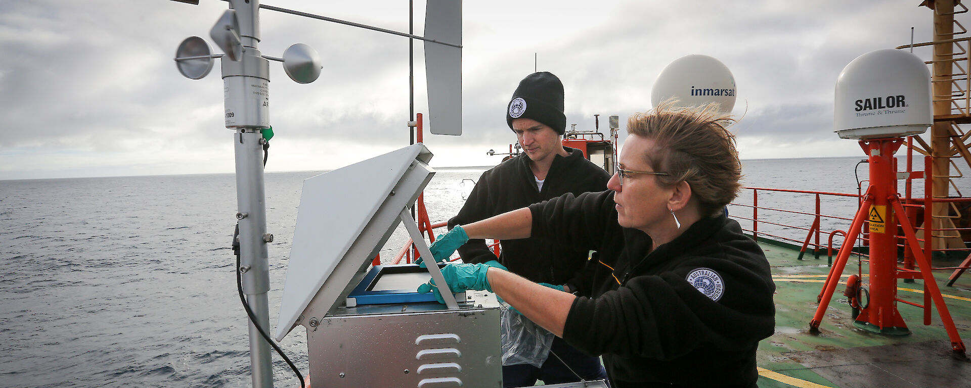Dr Alan Griffiths of ANSTO, and Professor Clare Murphy of the University of Wollongong, changing a filter on a high volume air sampler on the deck of the Aurora Australis.