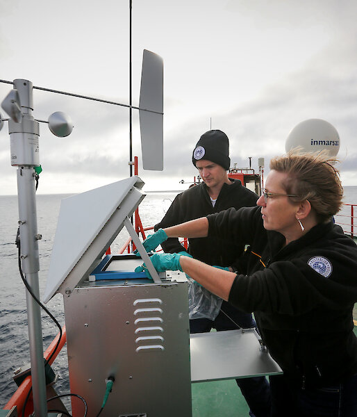 Dr Alan Griffiths of ANSTO, and Professor Clare Murphy of the University of Wollongong, changing a filter on a high volume air sampler on the deck of the Aurora Australis.