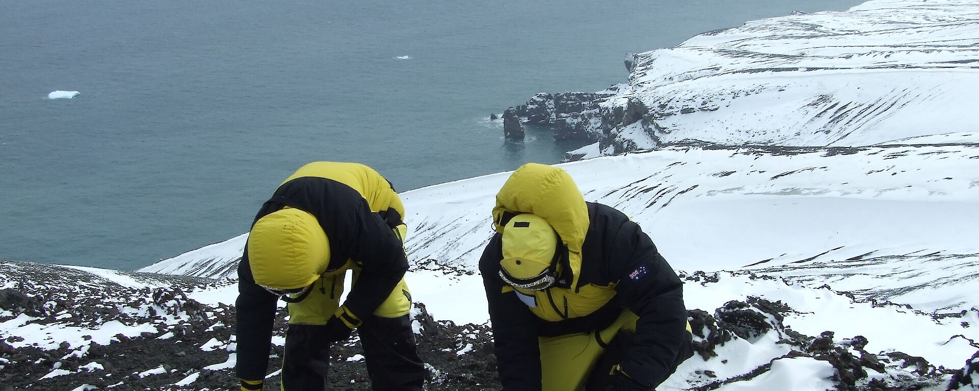 Two scientists in down jackets taking samples from a geothermal area.