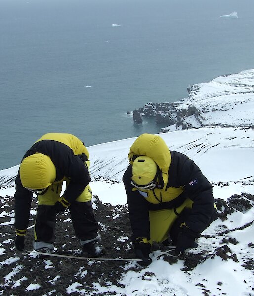 Two scientists in down jackets taking samples from a geothermal area.