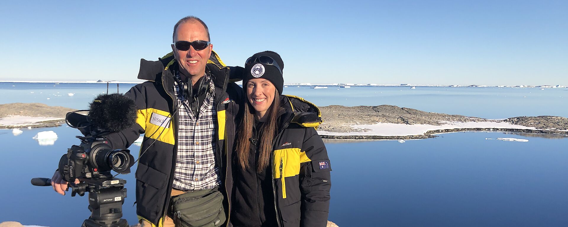 Behind the News team, Peter Curtis and Emma Davis standing on a rock overlooking a bay at Casey.